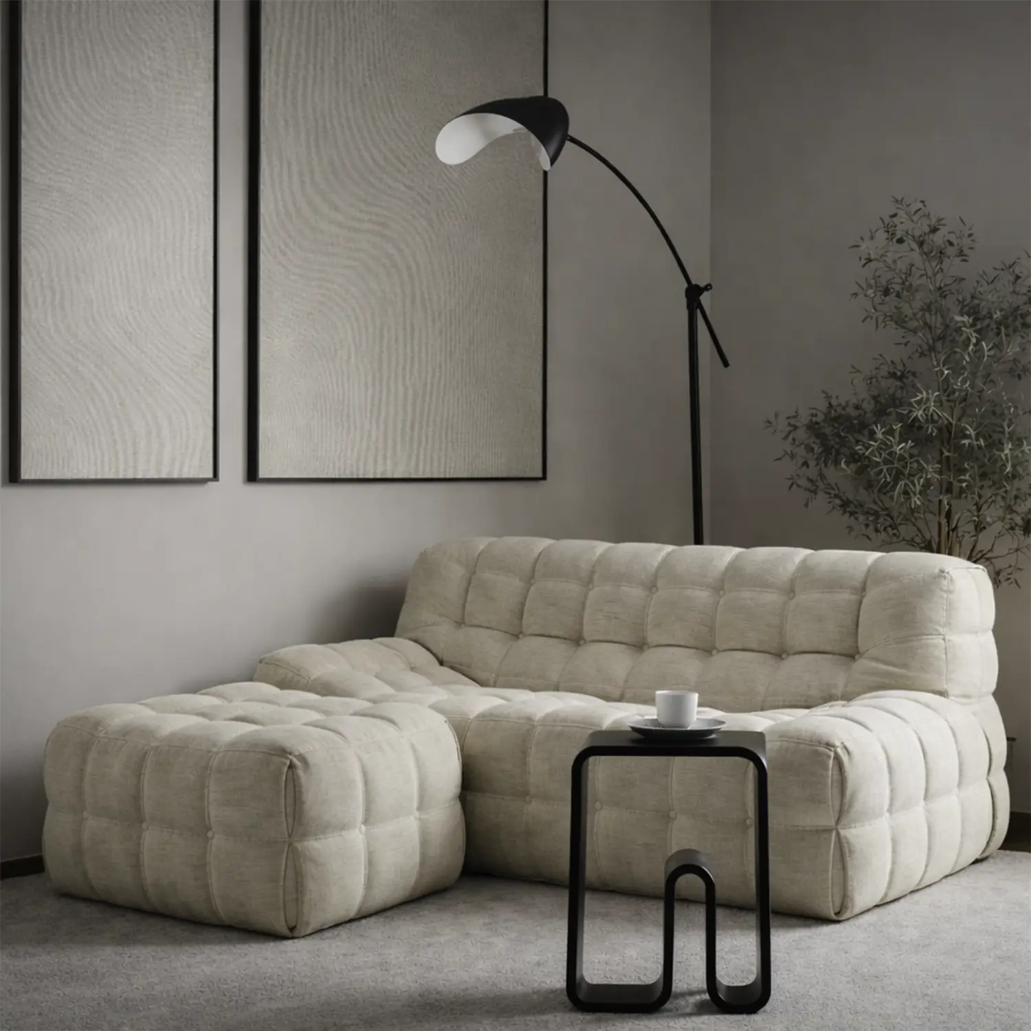 Modern beige tufted sectional sofa with matching ottoman, black side table holding a white cup and saucer, black arc floor lamp, and a green plant against a light gray wall with two abstract framed artworks.