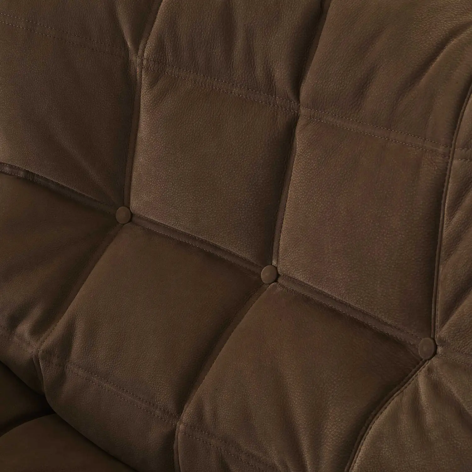 Close-up of tufted brown leather upholstery with stitched square patterns and button details.