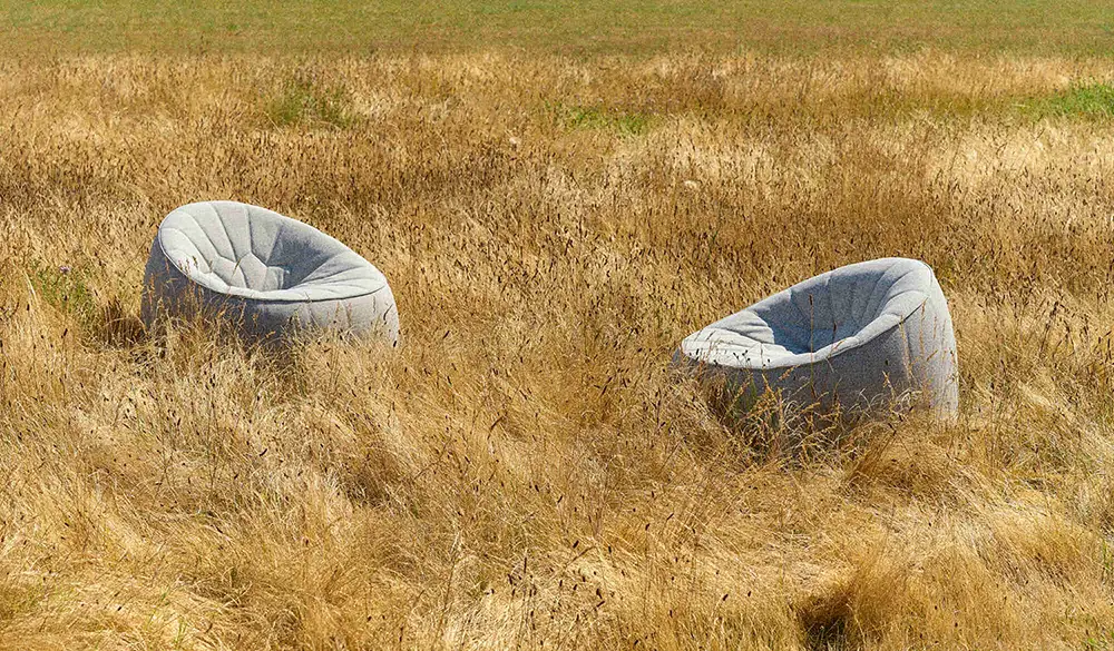 Two modern gray armchairs placed in tall dry grass field under natural daylight.