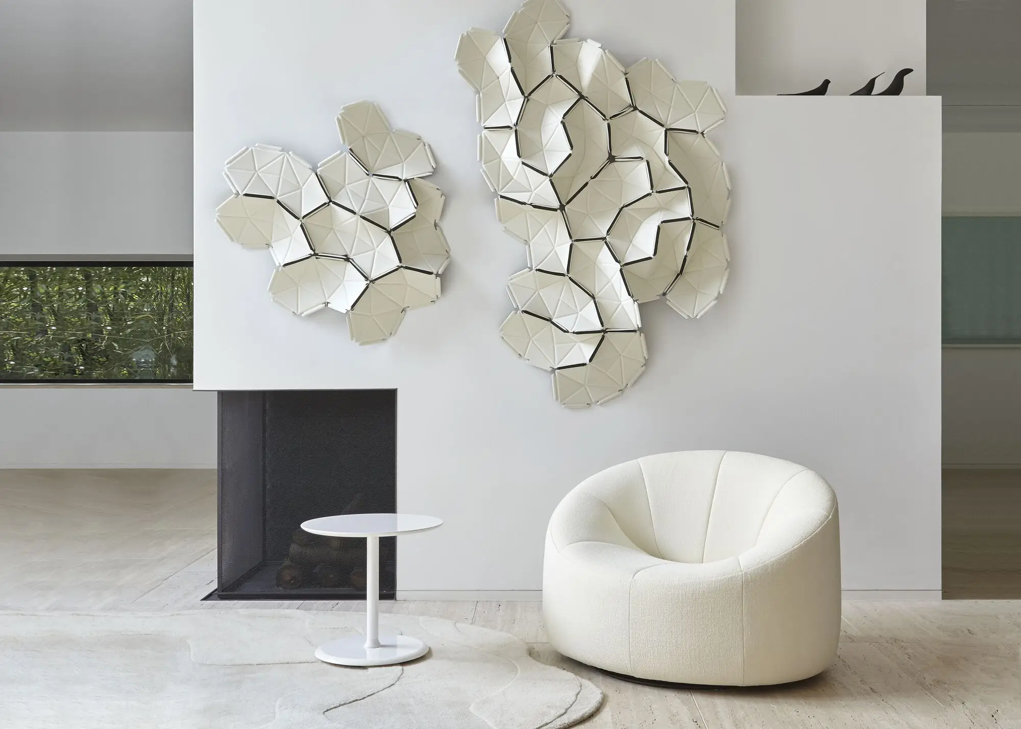 Modern minimalist living room with a white rounded armchair, a small white side table, abstract geometric wall art, and a fireplace.