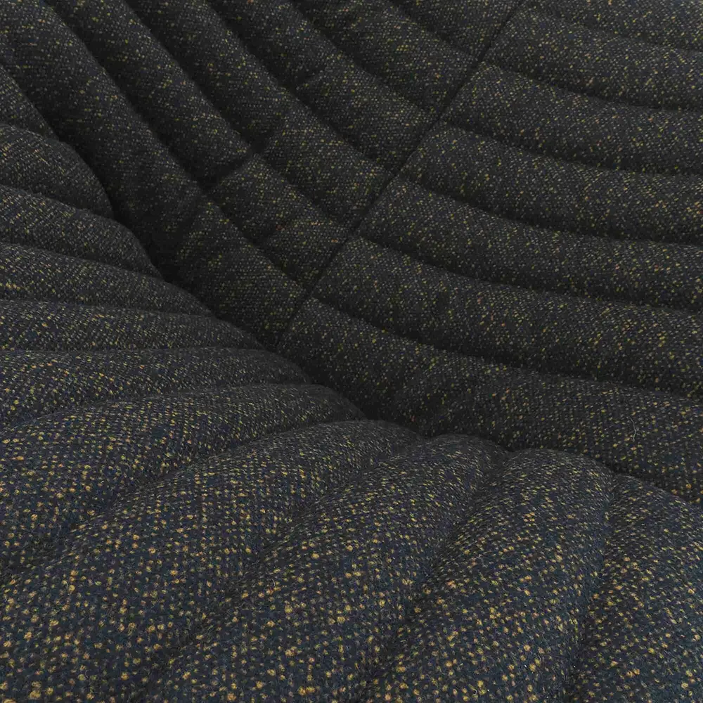 Close-up of a dark upholstery fabric with a textured weave and dimpled, padded surface.