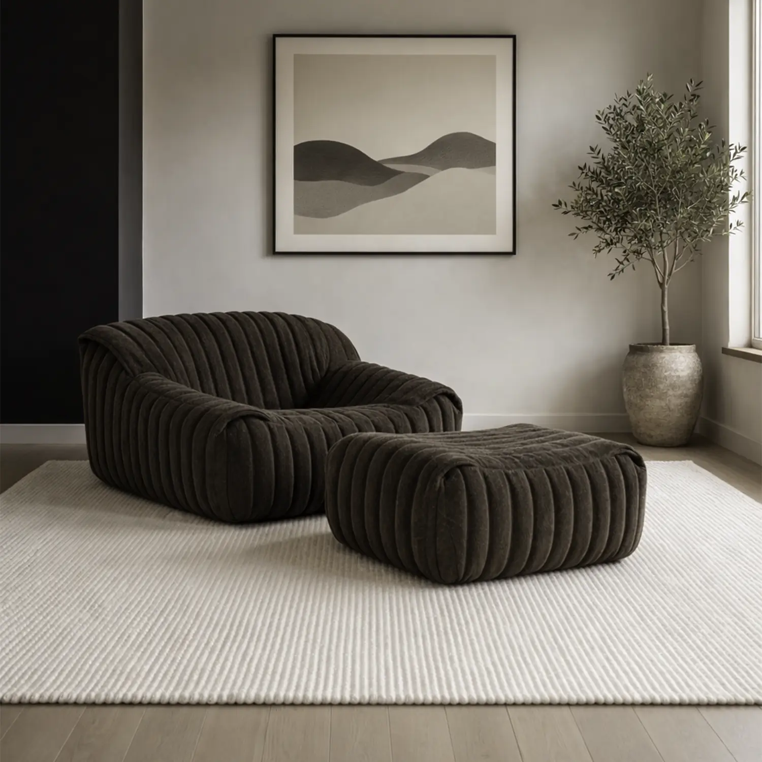 Modern living room with a dark brown ribbed lounge chair and matching ottoman on a light textured rug, a framed abstract landscape print, and a potted olive tree near a window.