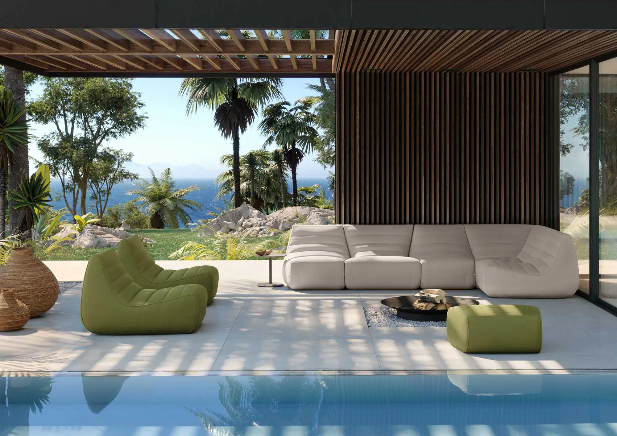 Modern outdoor seating area with a beige sectional sofa, two green lounge chairs, a green ottoman, and a fire pit beside a pool with lush greenery and ocean in the background.