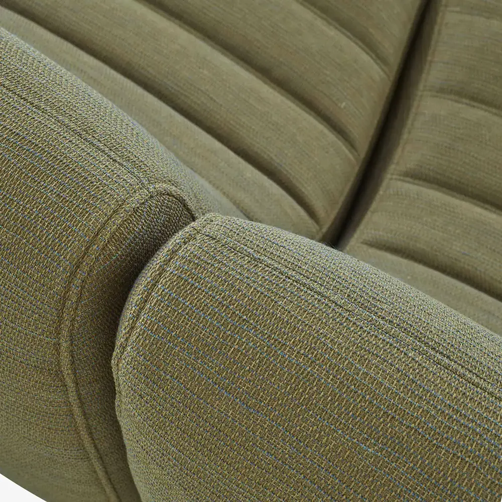 Close-up of olive green fabric upholstery on a cushioned sofa armrest and backrest with piped edges and ribbed stitching.