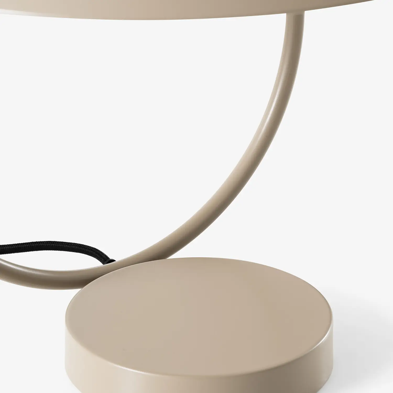 Close-up of a taupe-colored round metal base and curved frame of a modern table lamp with a black cord.