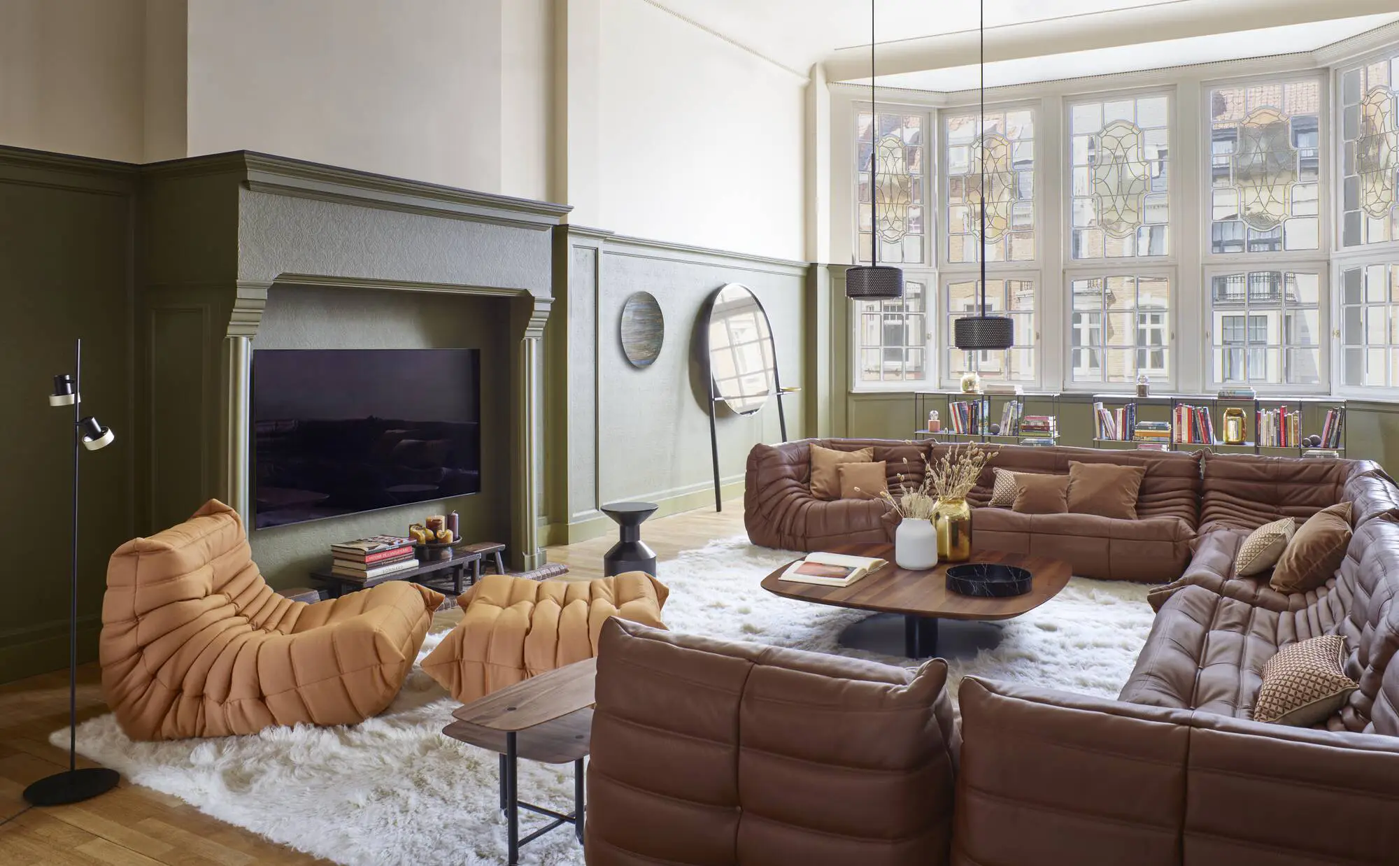 Spacious living room with brown leather sectional sofas, orange lounge chair, large windows with decorative glass, and a coffee table on a white shag rug.