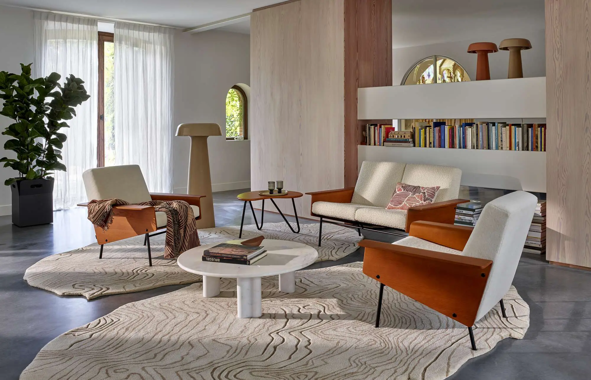 Modern living room with beige upholstered wood armchairs, a matching loveseat, circular coffee tables, and textured abstract rugs.
